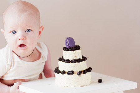 Baby boy with  small cake on three floors decorated  mulberry and purple macaroon on top.