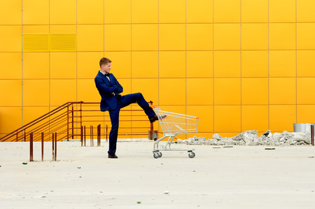 A man in a blue suit with an empty  shopping  cart outdoors.