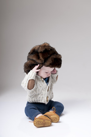 Funny baby boy in a winter fur hat cover gray background.の写真素材
