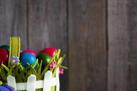 Easter greeting card. Multicolored eggs in basket over wooden background with space for text.