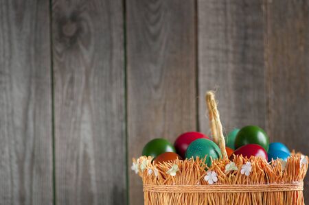 Easter greeting card. Multicolored eggs in basket over wooden background with space for text.