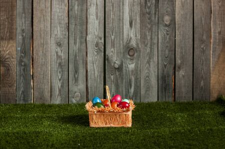 straw basket with Easter eggs on green artificial grass near a wooden fence - Greeting card with space for textの写真素材