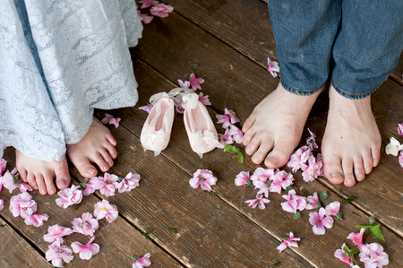 Family feet with baby's bootees on wooden brown boards among flowers. Birth expectation concept.の写真素材