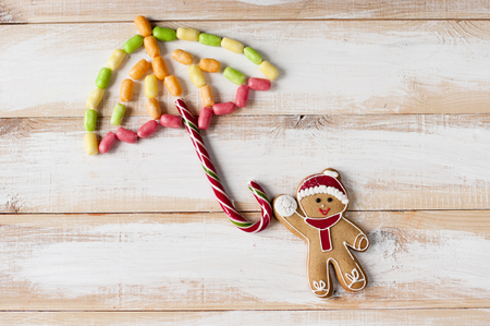Christmas composition from  gingerbread man with candies in form umbrella on wooden boards. Flat lay