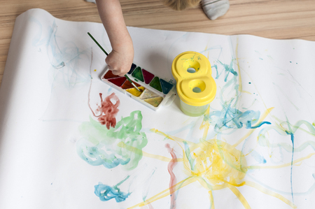 The kid draws a line with watercolor paints on white paper at homeの写真素材