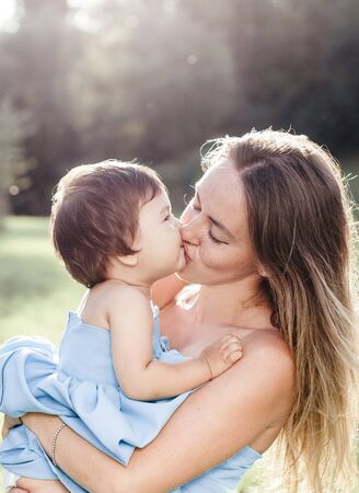 sunny portrait of kissing mother with small daughter in blue dressesの写真素材