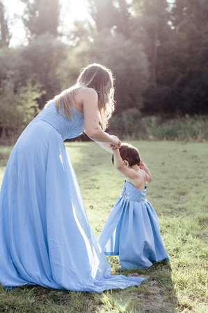 Mom with daughter in blue long indentical dresses on grass in forestの写真素材