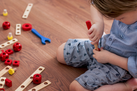 little boy twists wooden screwdriver screw,  sitting on the floorの写真素材