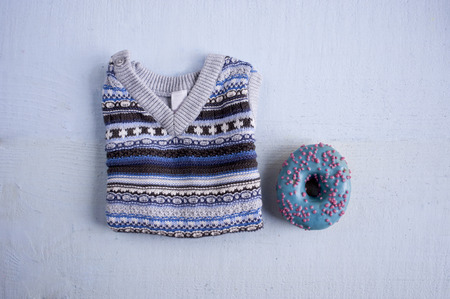 blue knitted waistcoat for a baby with a blue glazed donut. Flat lay on blue bckground.の写真素材