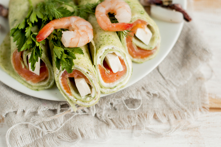 green pancakes stuffed with salmon, melted cheese, decorated with shrimps and parsley.の写真素材