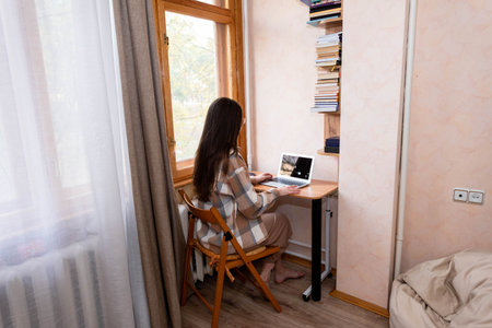 Freelancer girl with long hair working at home on a laptop near the windowの写真素材