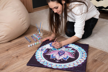 Woman with long dark hair paints a mandala with watercolors on the floorの写真素材