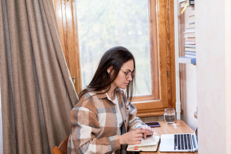 Freelancer girl with long hair working at home on a laptop near the windowの写真素材