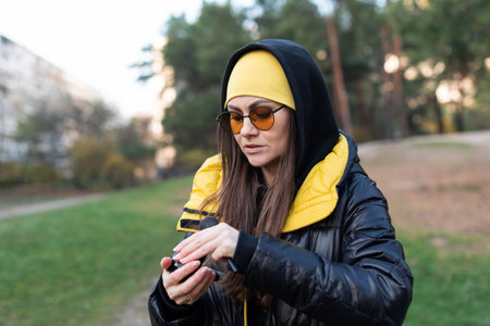 A woman in orange glasses fixes her makeup outdoors - uses a mirror and a brushの写真素材