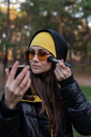 A girl in orange glasses fixes her makeup on the street - uses a mirror and a brushの写真素材