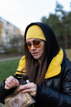 A girl in orange glasses fixes her makeup on the street - uses a mirror and a brushの写真素材