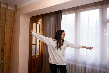 Happy, energetic girl in a white sweatshirt and black leggings dancing at homeの写真素材
