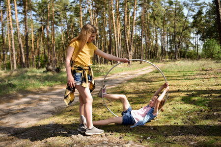 Cute school-age girls playing with a gymnastic metal hoop in the forest on a trailの写真素材