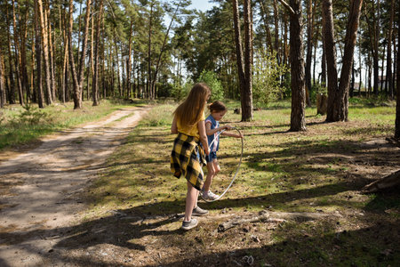Cute school-age girls playing with a gymnastic metal hoop in the forest on a trailの写真素材