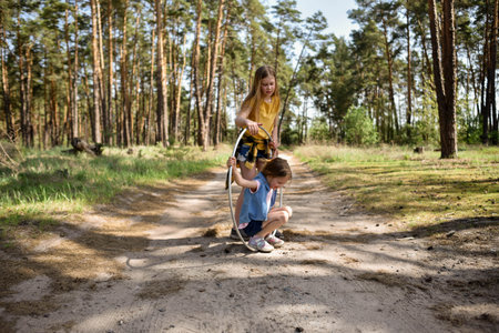 Cute school-age girls playing with a metal hoop in the forest on a trailの写真素材