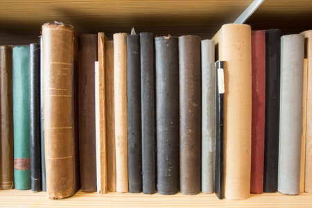 Many old dusty books in a library on a wooden shelveの写真素材
