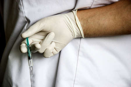 Doctor hand in white glove hold syringe with preparation jet from the needle. Medical man holding...