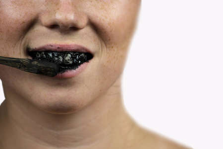 young woman brushing her teeth with a black tooth paste with active charcoal, and black tooth brush...