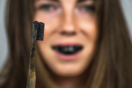 young woman brushing her teeth with a black tooth paste with active charcoal, and black tooth brush on white background for Teeth whiteningの写真素材