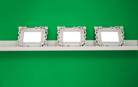 three white empty photo frames on a green wall and wooden shelf, isolated, space for text or photo