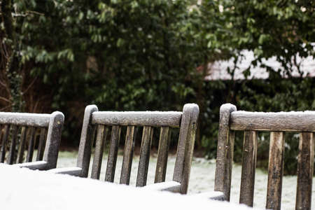 Wooden cozy garden chairs covered in snow in a backyard garden.の写真素材