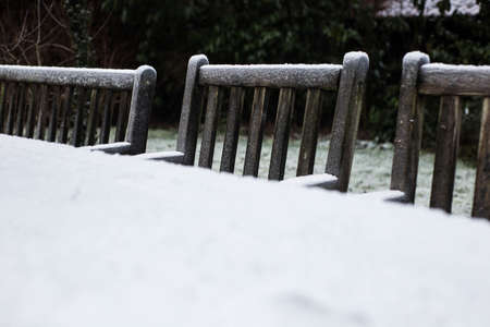 Wooden cozy garden chairs covered in snow in a backyard garden.の写真素材
