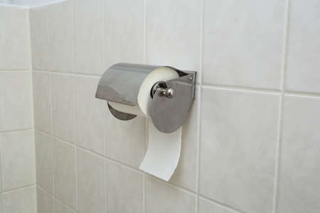 A white roll of soft toilet paper neatly hanging on a modern chrome holder on a light bathroom wall.の写真素材