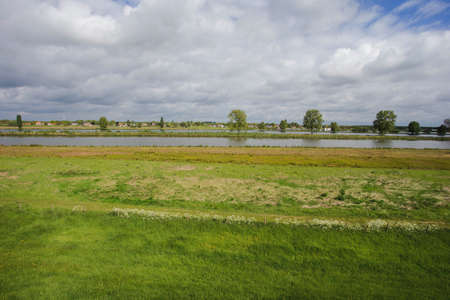 Beautiful view on a typical dutch landscape near the river Waal and water, green grass, meadows and trees on a sunny day in april, springtimeの写真素材