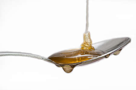 Honey dripping from a silver spoon on isolated white background food conceptの写真素材