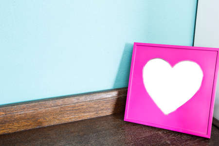 Pink heart picture frame on wood table with blue wall background, space for text close-upの写真素材
