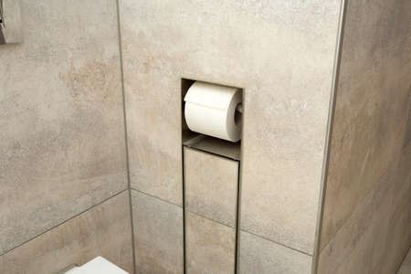 A white roll of soft toilet paper neatly hanging on a modern chrome holder in the wall close-upの写真素材