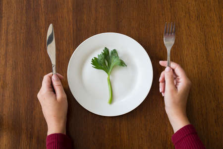 diet concept. one green vegetable on an empty white plate with woman hands celery on wood table healthy top viewの写真素材