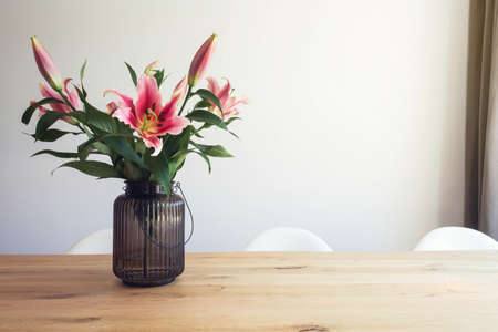 pink lily flowers in a vase on a wooden table in the interior against a white wall in modern room beautyの写真素材