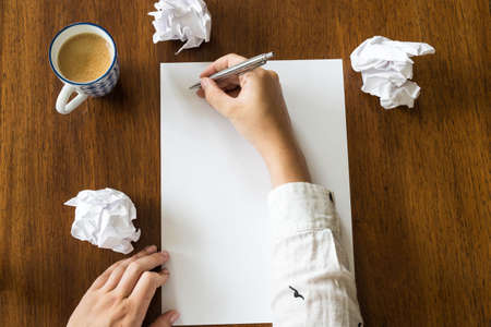 Blank sheet of paper and pen on bright wooden office desk with hands of a person close-upの写真素材