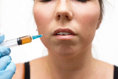 Ordinary woman receiving a botox injection in her lips, close up beauty treatment concept isolated on whiteの写真素材