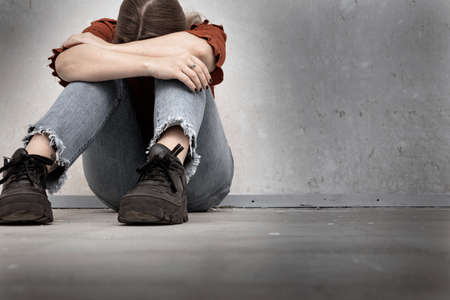 Young woman cries and sitting near a empty wall, lonely sad and depressed girl holding her head down