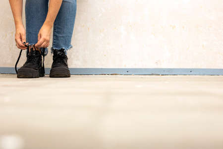 young woman hands tying shoelaces. black sneakers in white room, near white wall