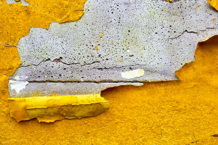 Concrete wall with yellow, orange peeling paint old cracked damaged rough bright background texture