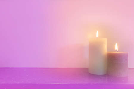 Two burning candles in front of purple pink background, light pastel colors modern design, space for text backgroundの写真素材