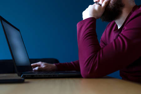 Young man surfs the internet on his laptop late at night with blue background, working late with...