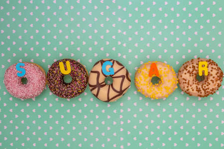 Group of delicious colorful glazed donuts near green background with white hearts pattern and the word sugarの写真素材