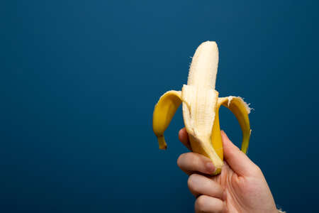 Peeled yellow banana fruit near blue background in hand, healthy concept close-upの写真素材