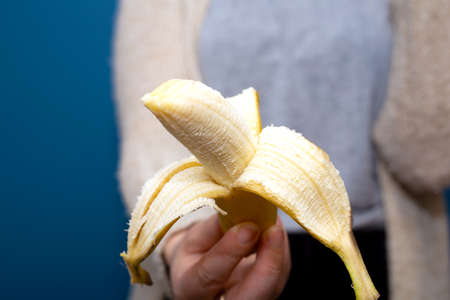Person holding a yellow banana fruit in hand near blue background, giving away healthy concept...