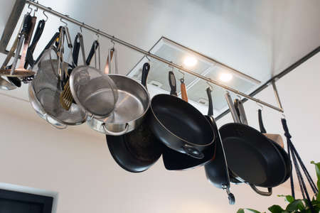 Stainless steel cookware , kitchenware set hanging on a rack on the wall, frying pans and saucepan in modern homeの写真素材