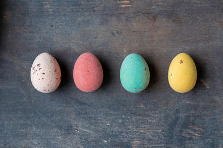 Dyed colorful easter eggs in a row on a vintage wooden background texture, soft pastels modern...